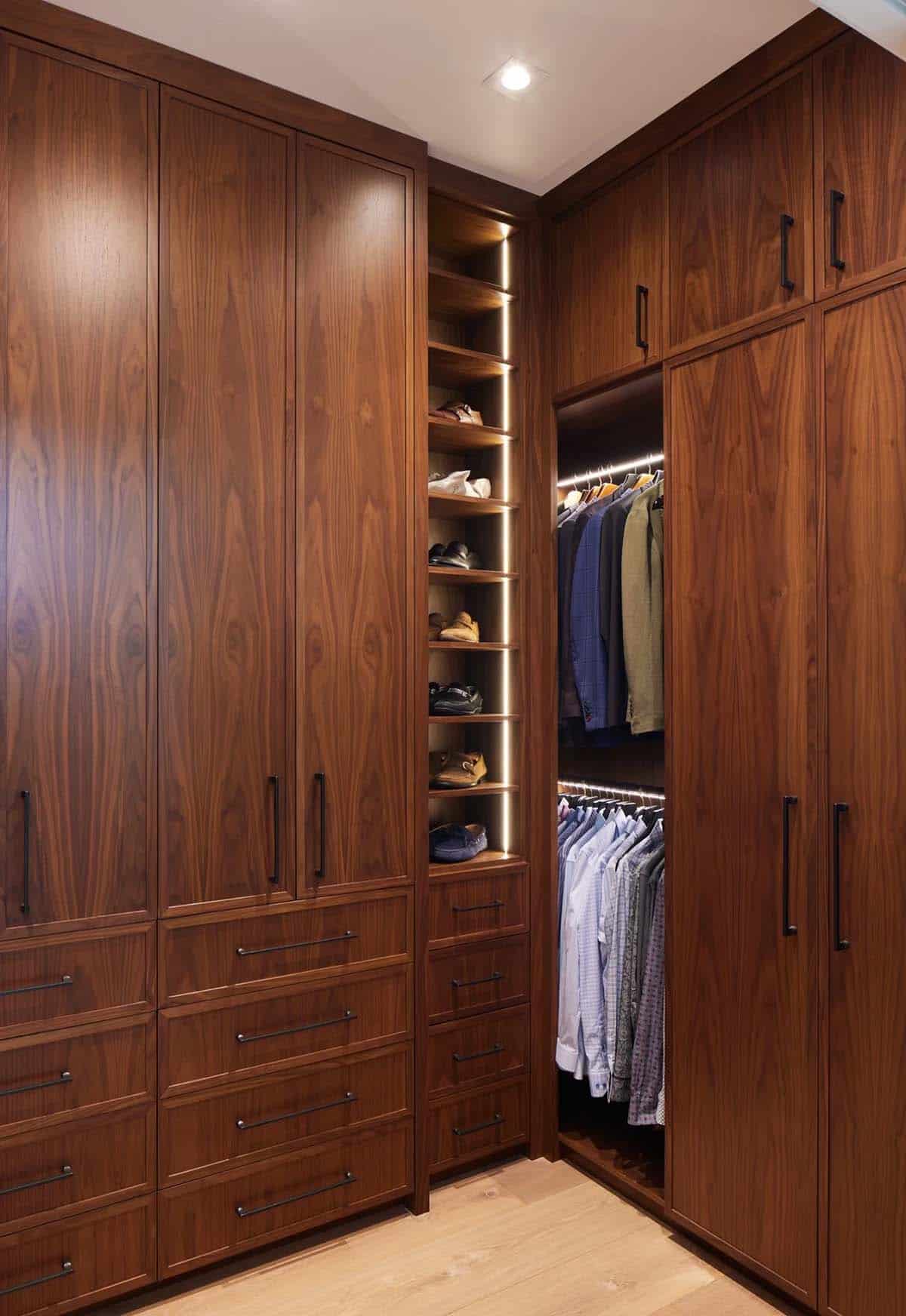 Walk-in closet with walnut cabinetry, lit shoe shelving, and hanging clothes