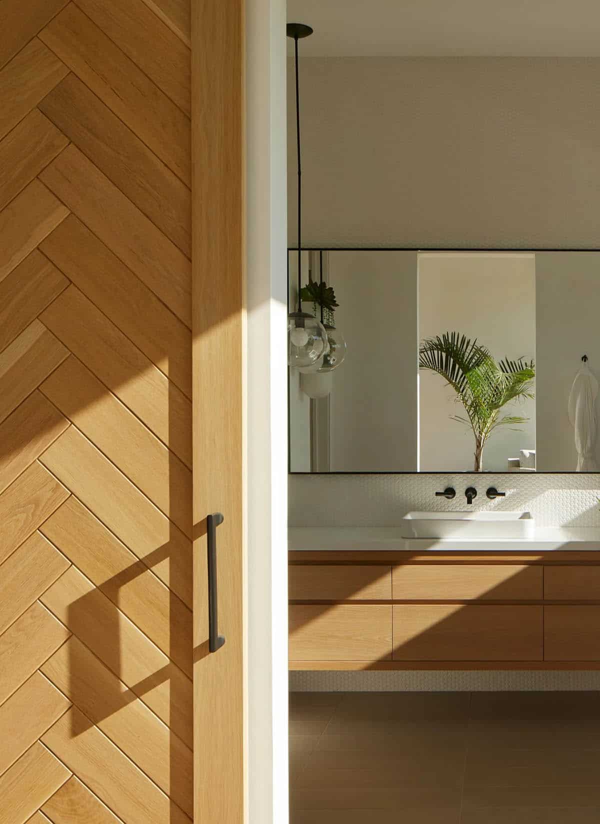Herringbone wood sliding door beside bathroom vanity with palm plant reflection