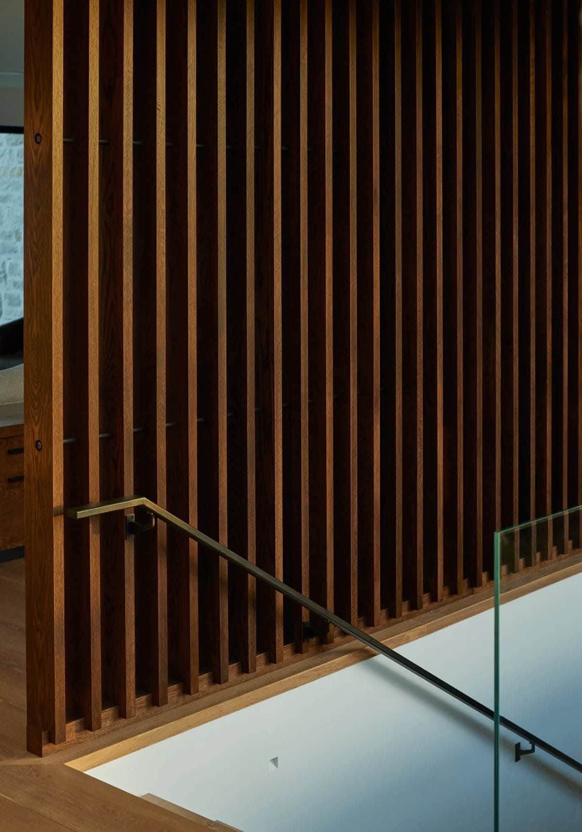 Detail of vertical wood slat wall with brass stair handrail