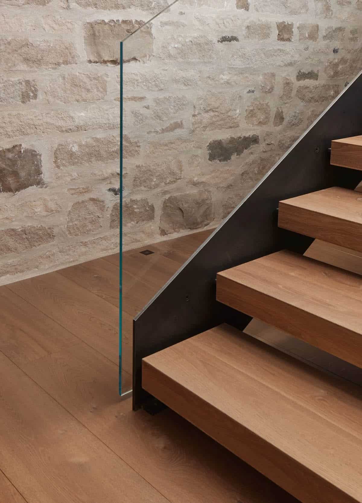 Floating wood staircase against stone wall with glass railing