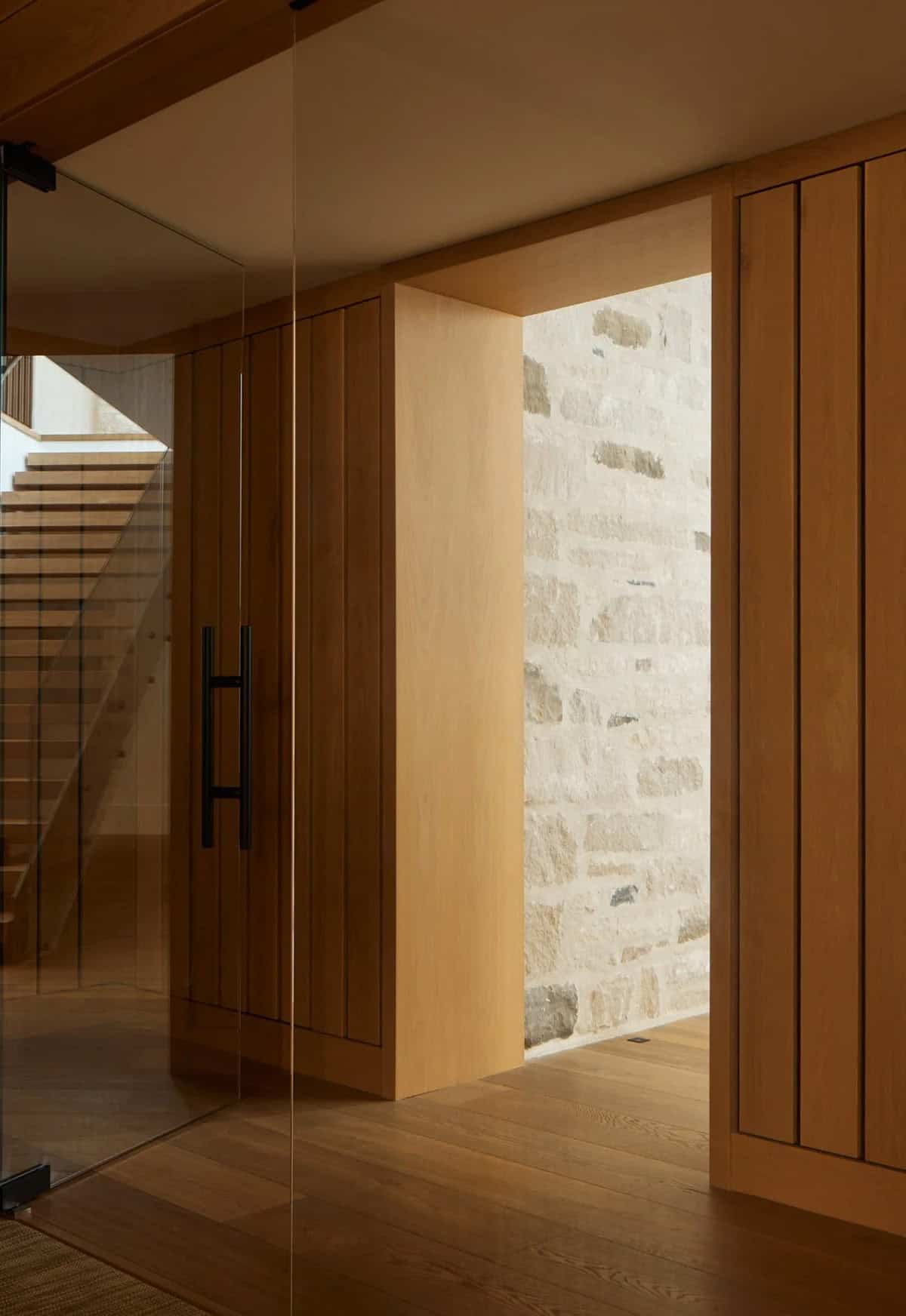 Wood-paneled hallway with glass door and view of stone wall niche