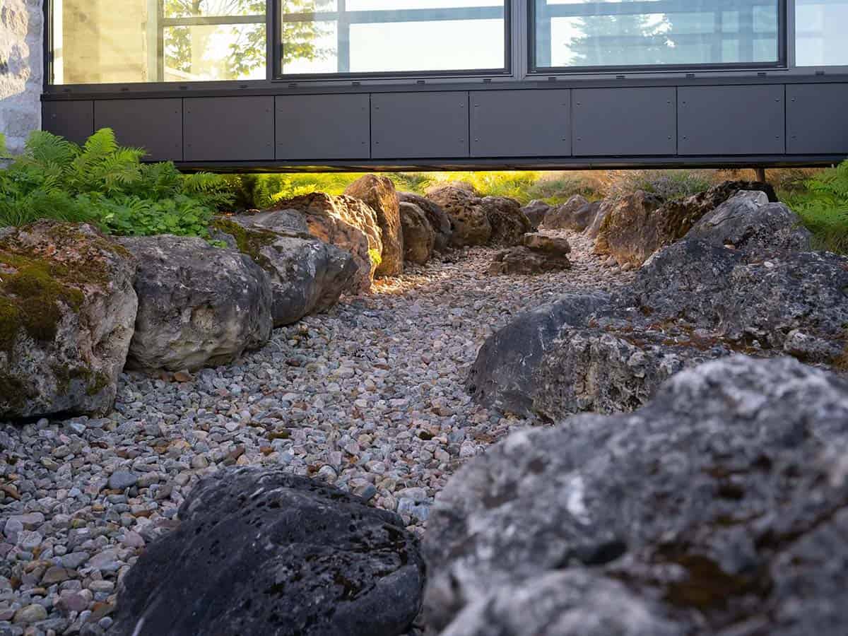 Dry creek bed landscaping with boulders beneath cantilevered black window wall