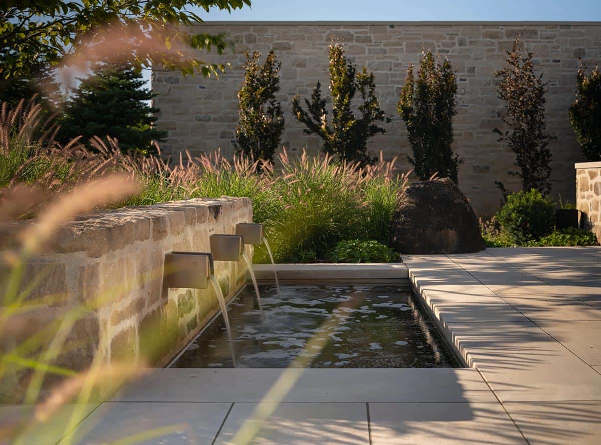 Stone wall water feature with three spouts flowing into reflecting pool