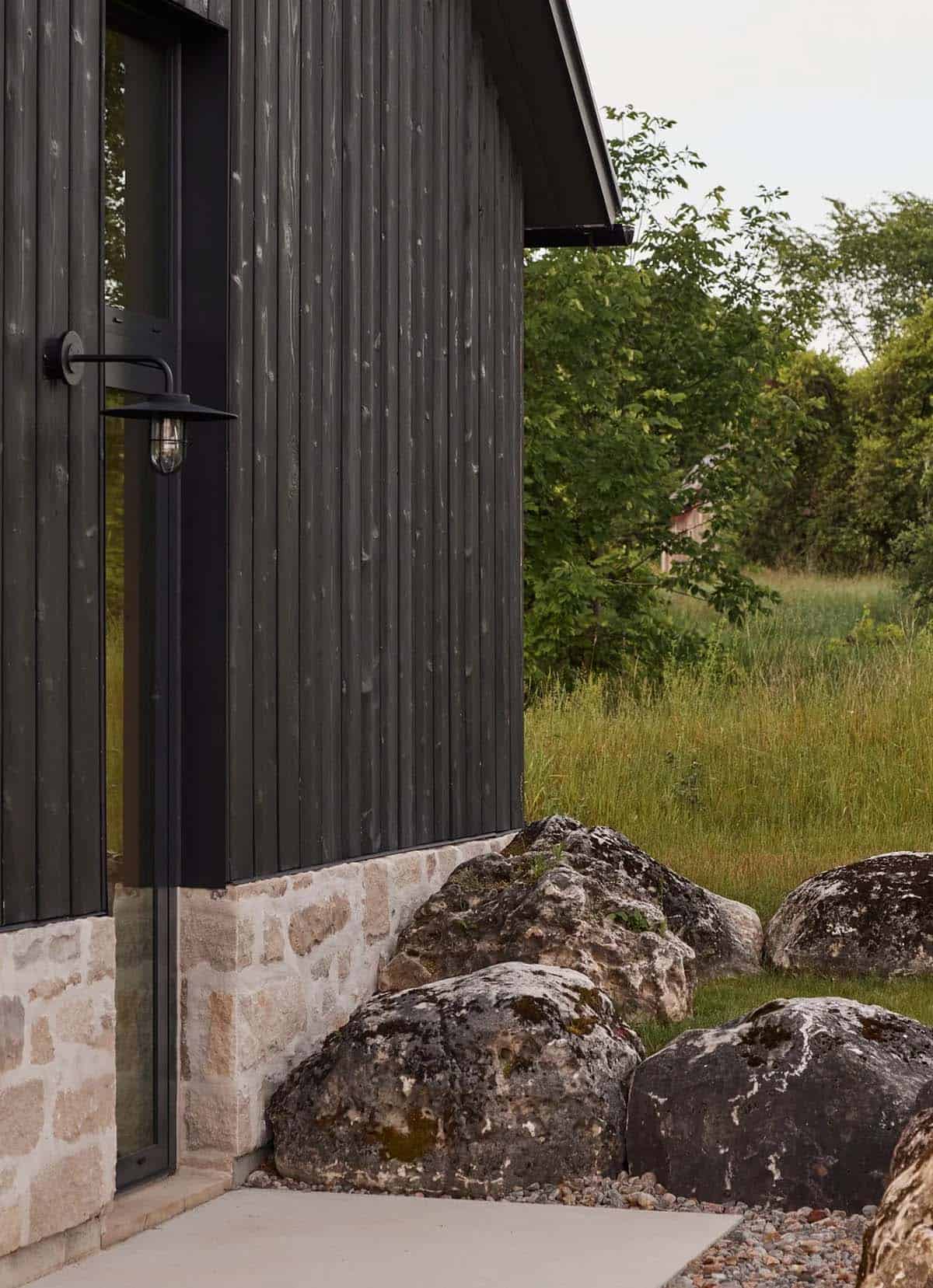 Detail of black wood-clad garage pavilion corner with stone base and boulders