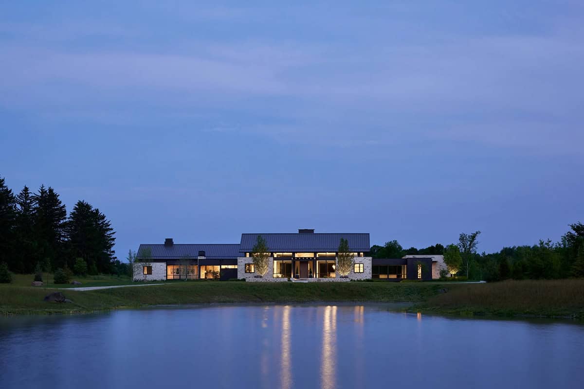Main home illuminated at dusk, reflected in pond under twilight sky
