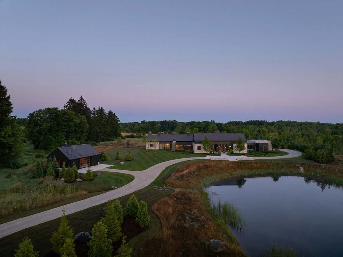 Aerial dusk view of home's pavilions, driveway, and pond amid forest