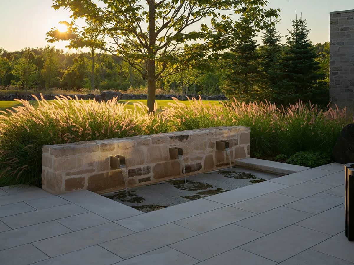 Stone water feature with triple spouts flowing into pool at sunset