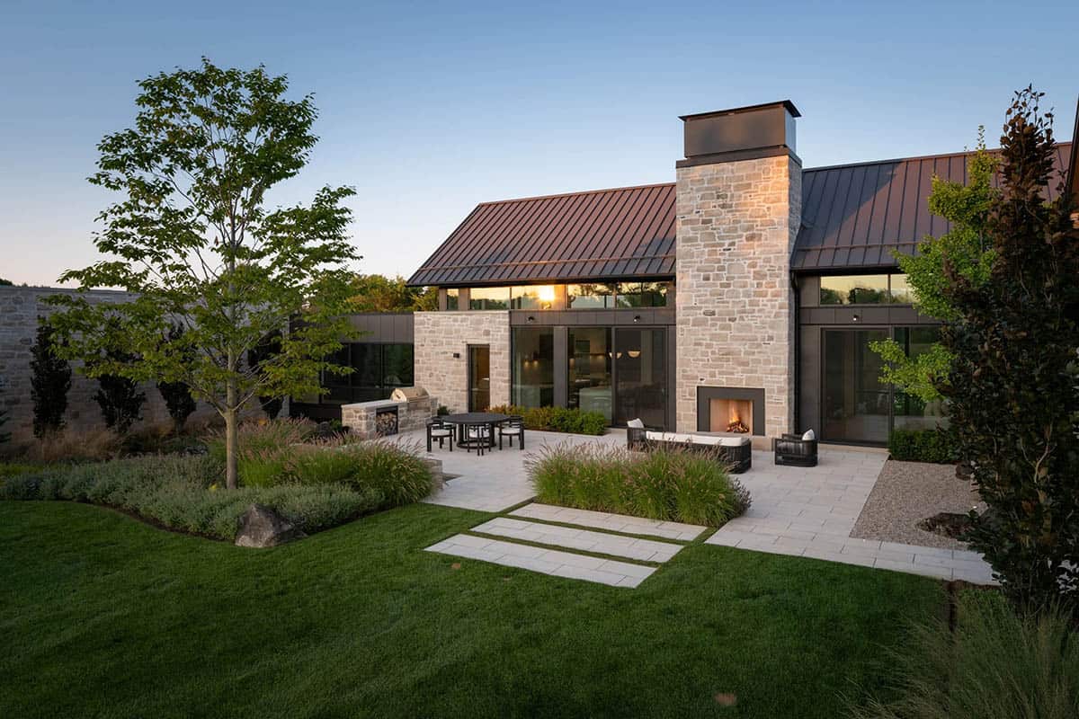 Rear patio with stone fireplace, outdoor seating, and manicured landscaping at dusk