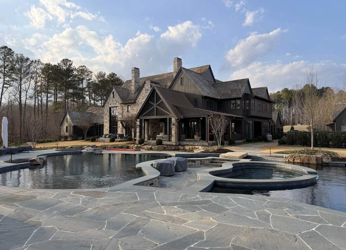 Stone and dark-timber European-style country estate with a freeform pool and spa at dusk