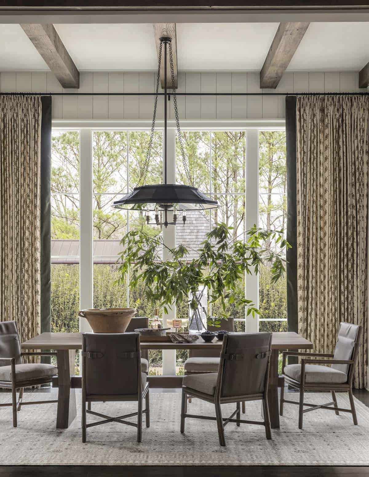 Dining room with leather-back chairs, wood beams, and floor-to-ceiling windows overlooking trees