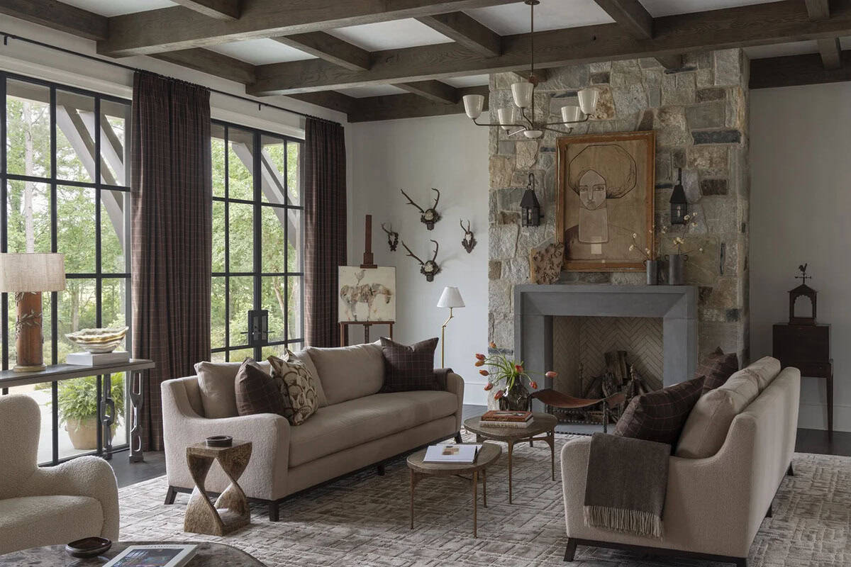 Living room with stone fireplace, beamed ceiling, and neutral sofas facing steel windows
