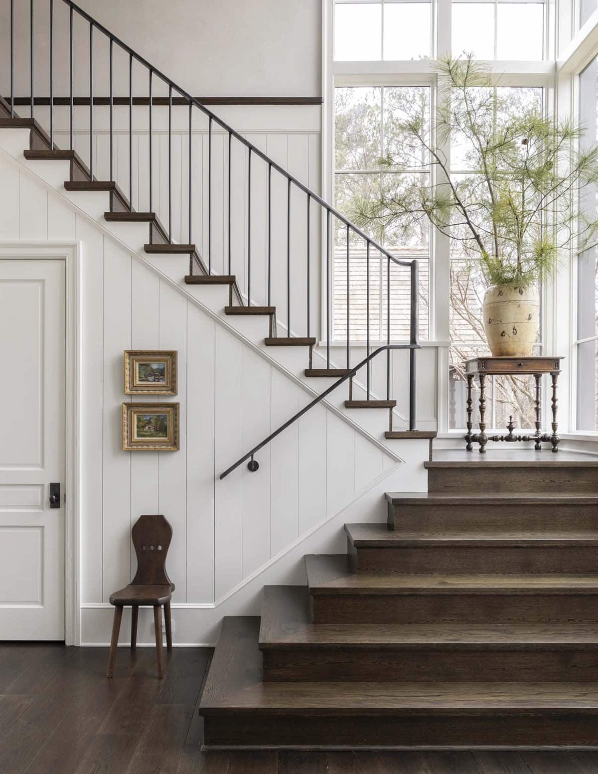 Wood staircase with iron railing beside a tall window and antique urn on a side table