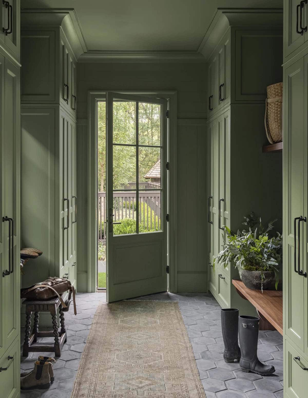 Green mudroom hallway with paneled cabinetry leading to a glass door