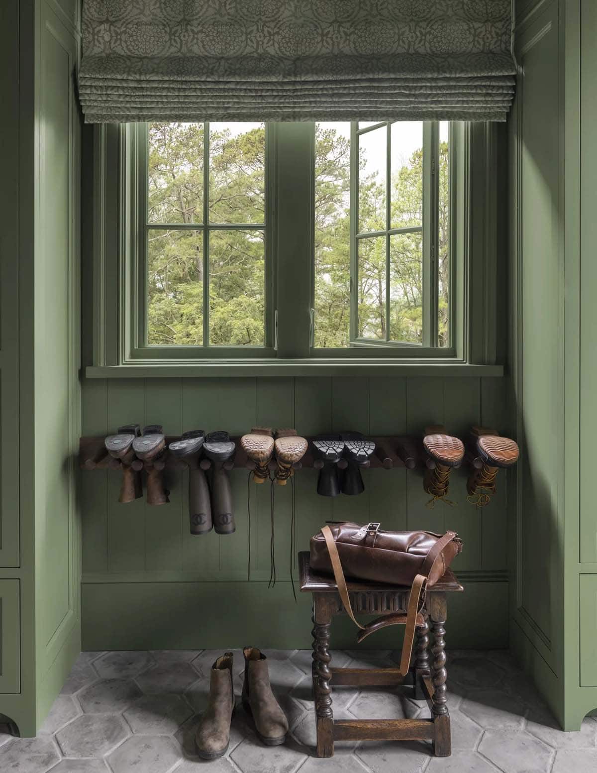Green mudroom nook with boot rack, patterned Roman shade, and antique bench