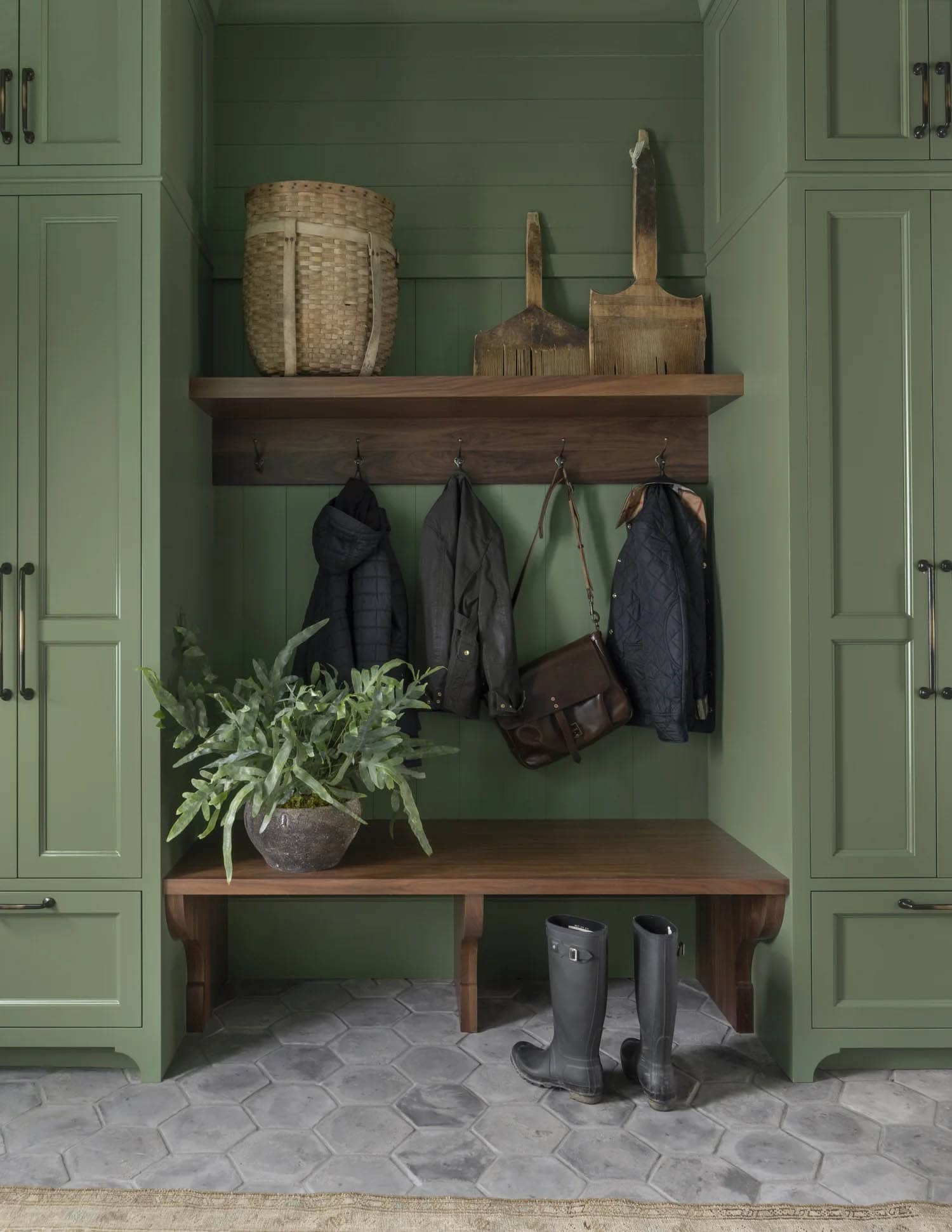 Green mudroom cubby with coat hooks, wicker basket, and rain boots