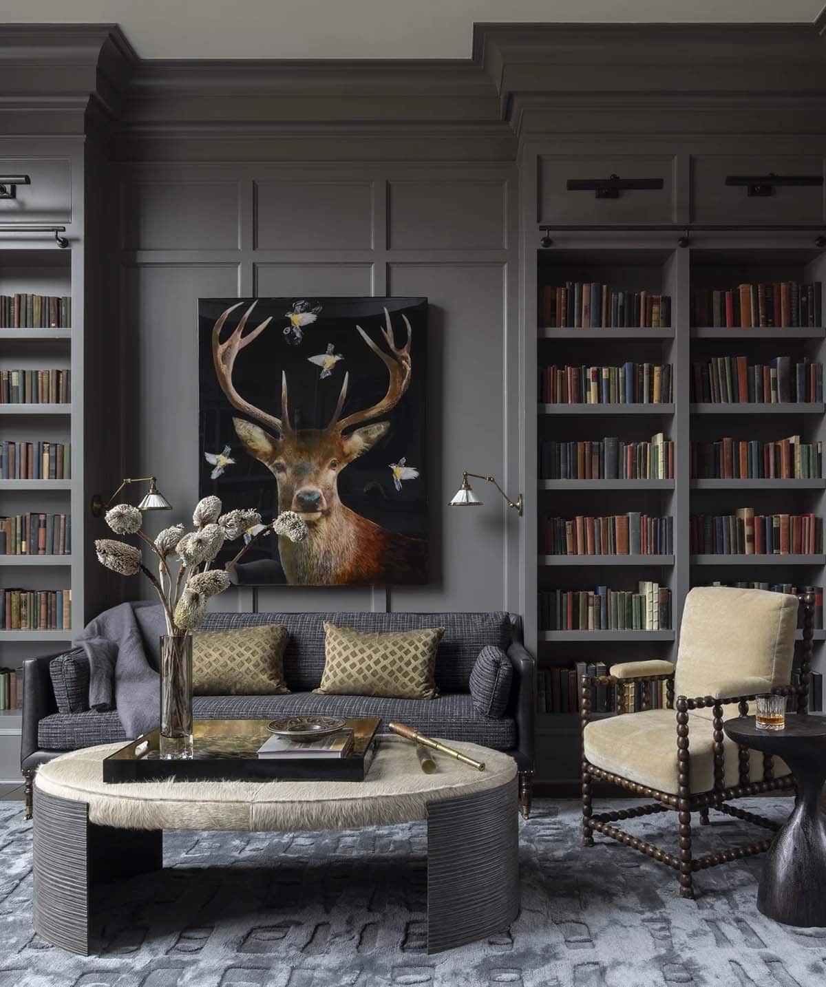 Dark paneled library with built-in bookshelves and a stag artwork above the sofa