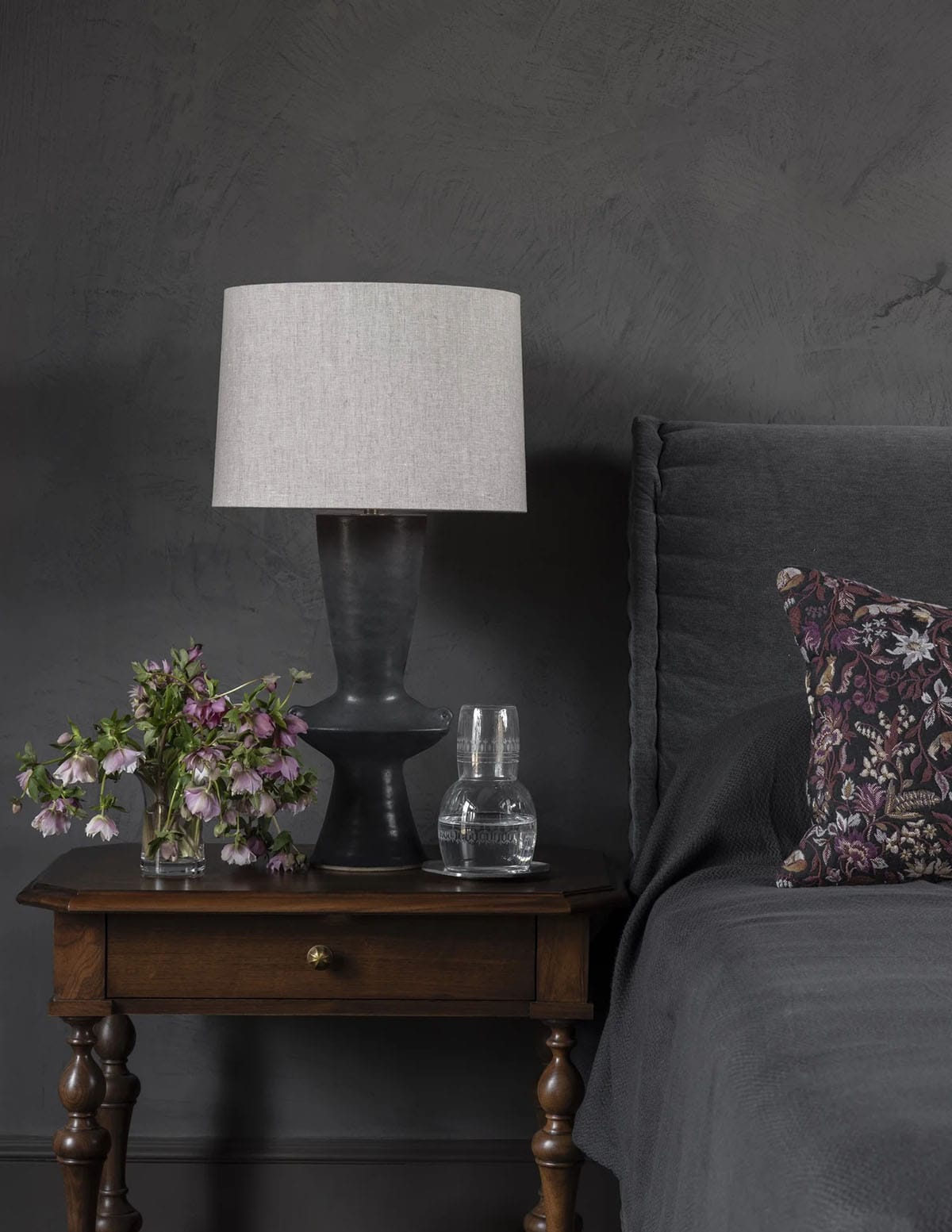 Dark bedroom nightstand vignette with black ceramic lamp and fresh-cut flowers
