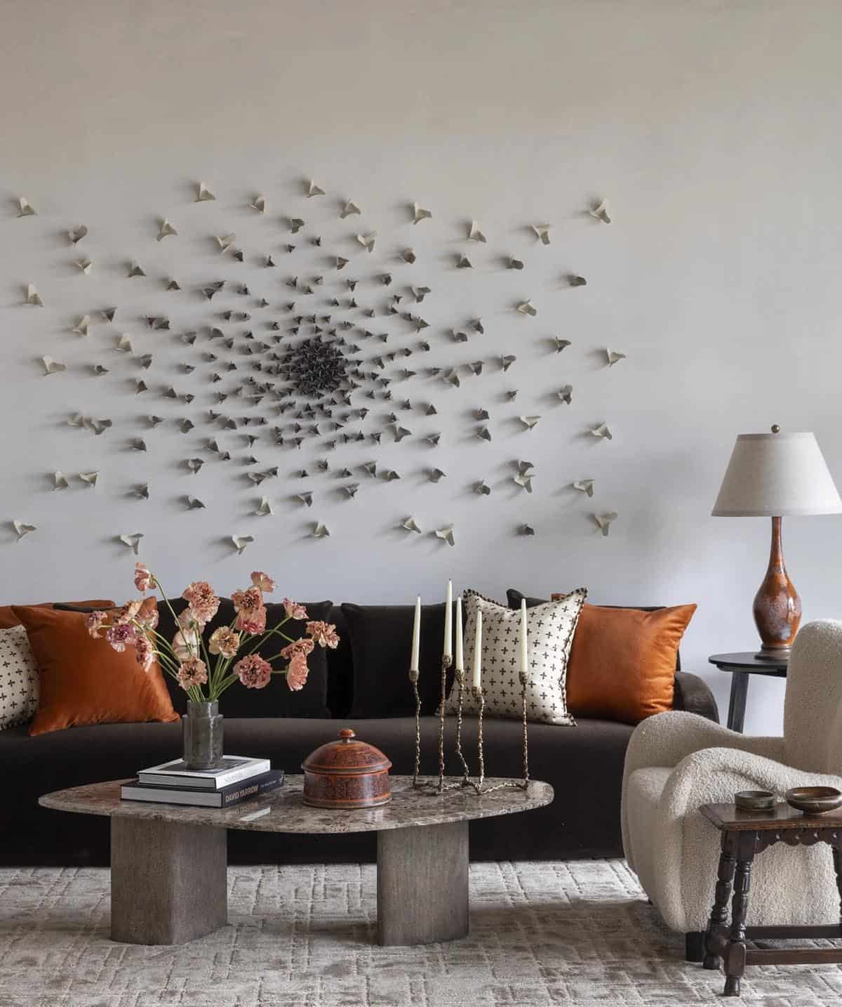 Living room with dark velvet sofa, rust-colored pillows, and a bird-flock wall sculpture
