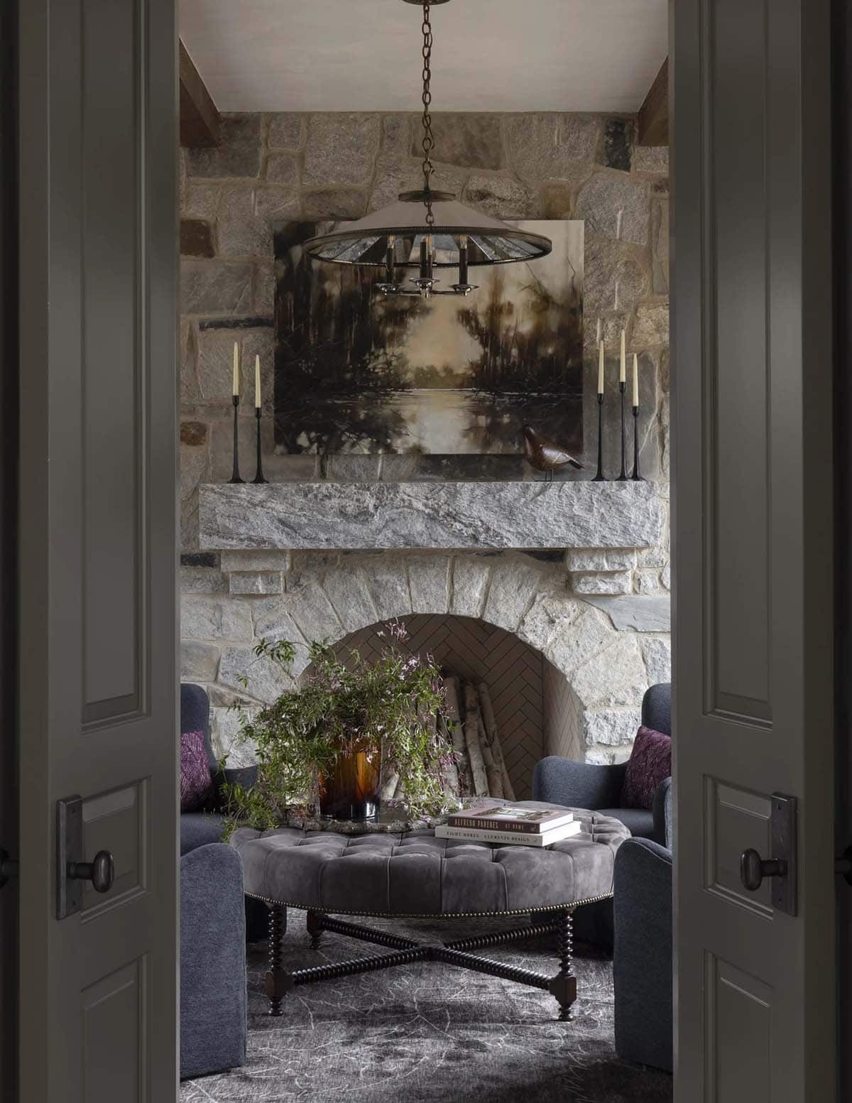 Sitting room seen through open doors with a stone fireplace and tufted round ottoman