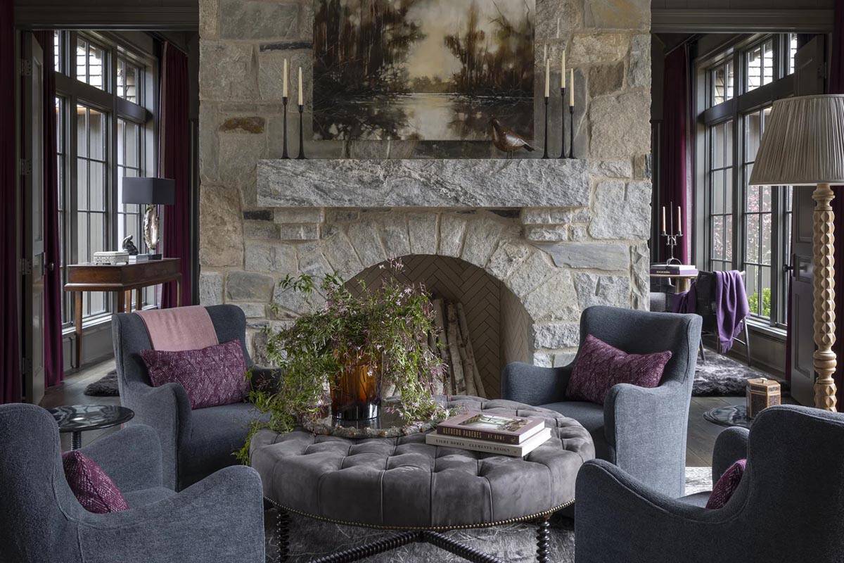 Sitting room with stone fireplace, four armchairs, and burgundy curtains at tall windows