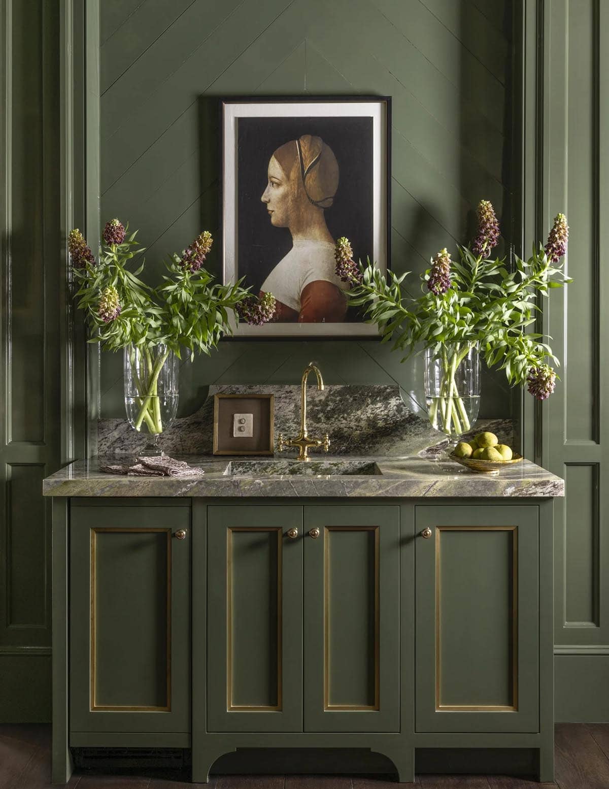 Green wet bar sink with marble backsplash, brass gooseneck faucet, and framed portrait