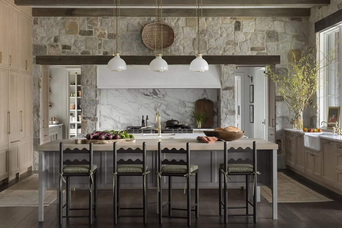 Kitchen island with scalloped-trim barstools facing a stone hood and marble backsplash