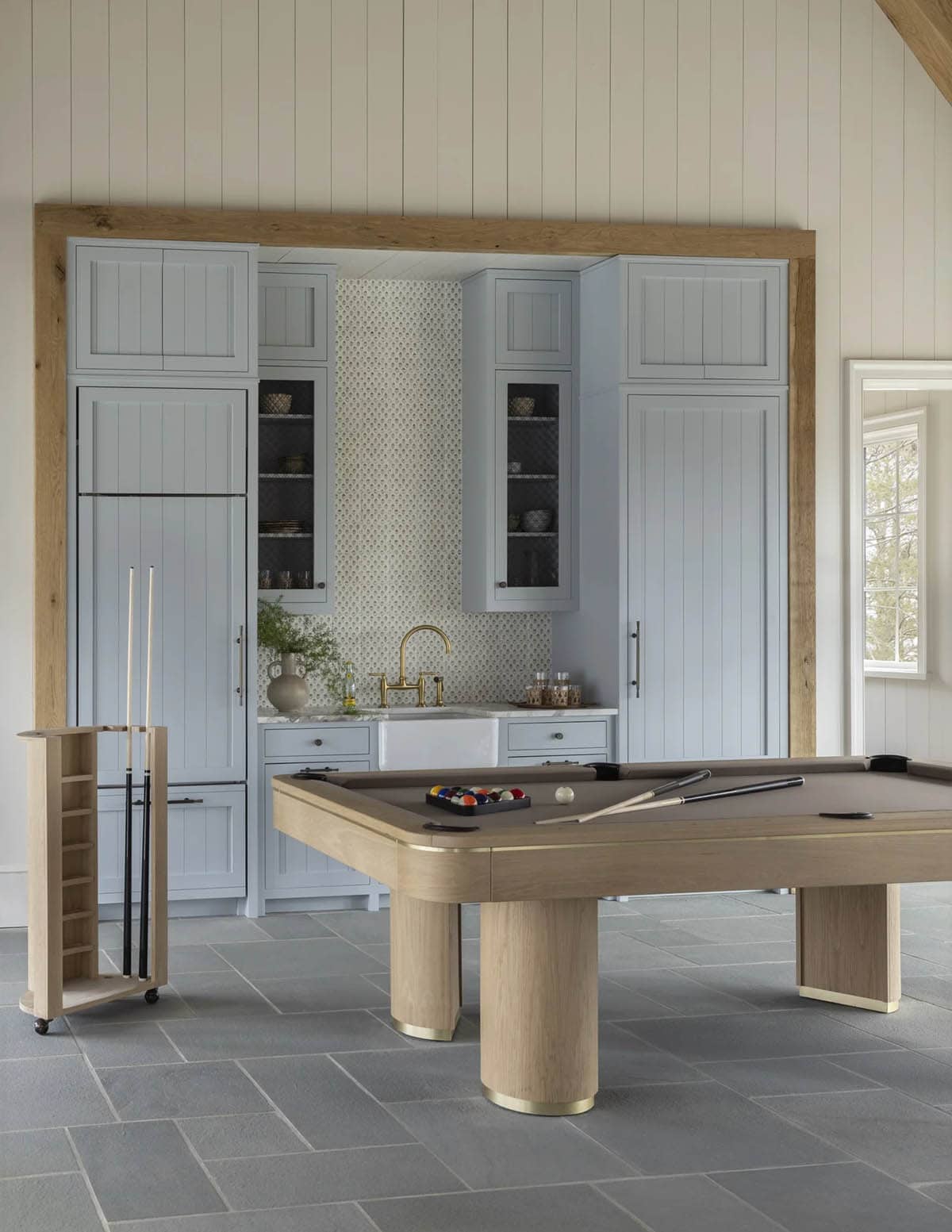 Game room with a wooden pool table, cue rack, and pale blue wet bar cabinetry