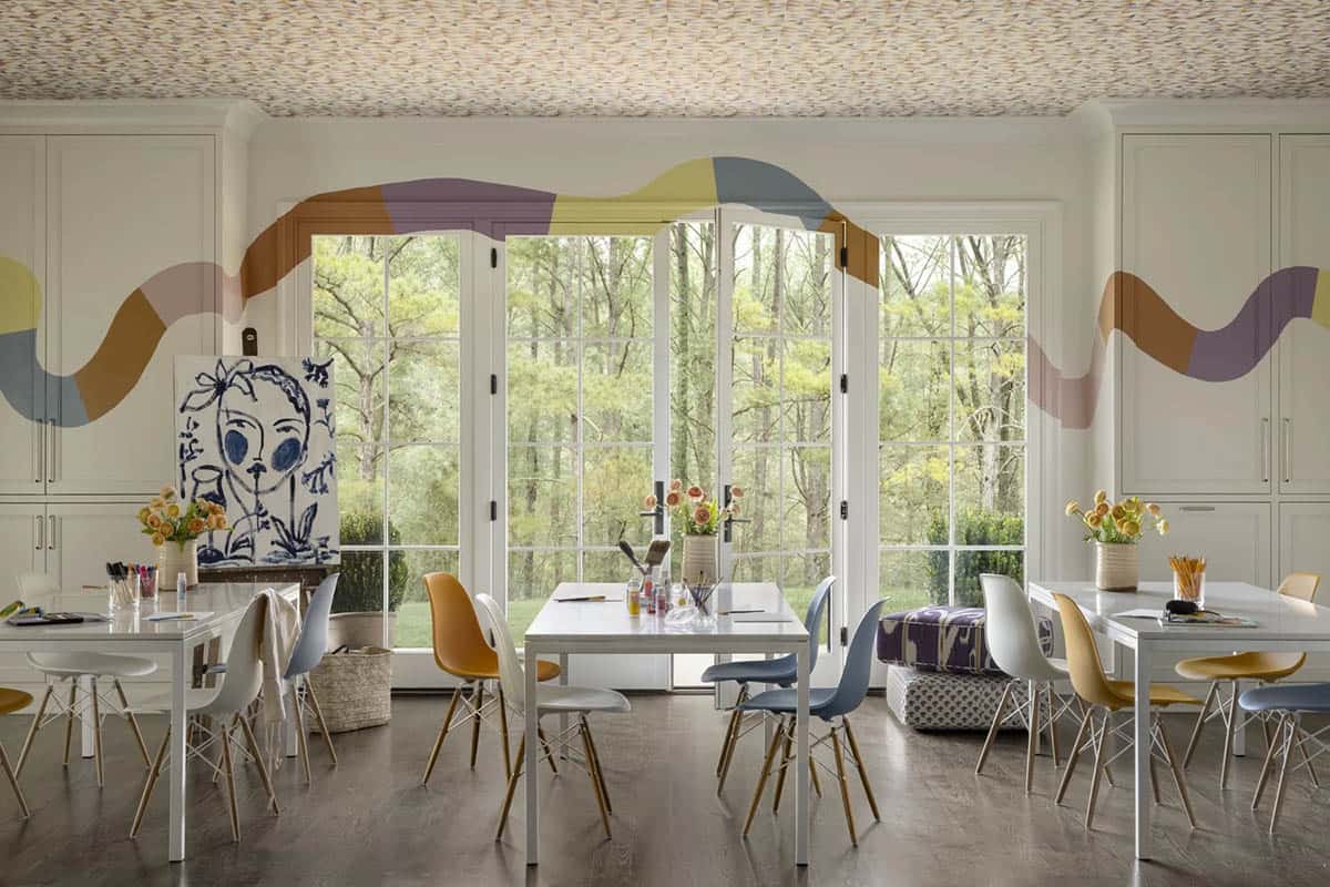 Colorful art/craft room with white tables, mismatched Eames chairs, and a wavy painted mural