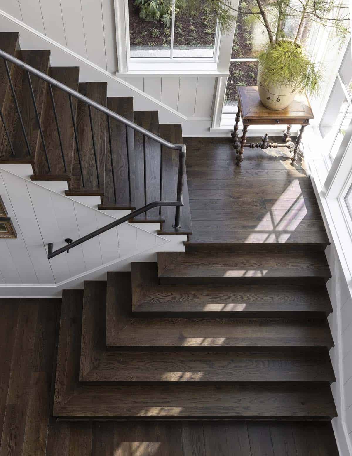 Overhead view of a wood staircase landing with an antique table and potted pine
