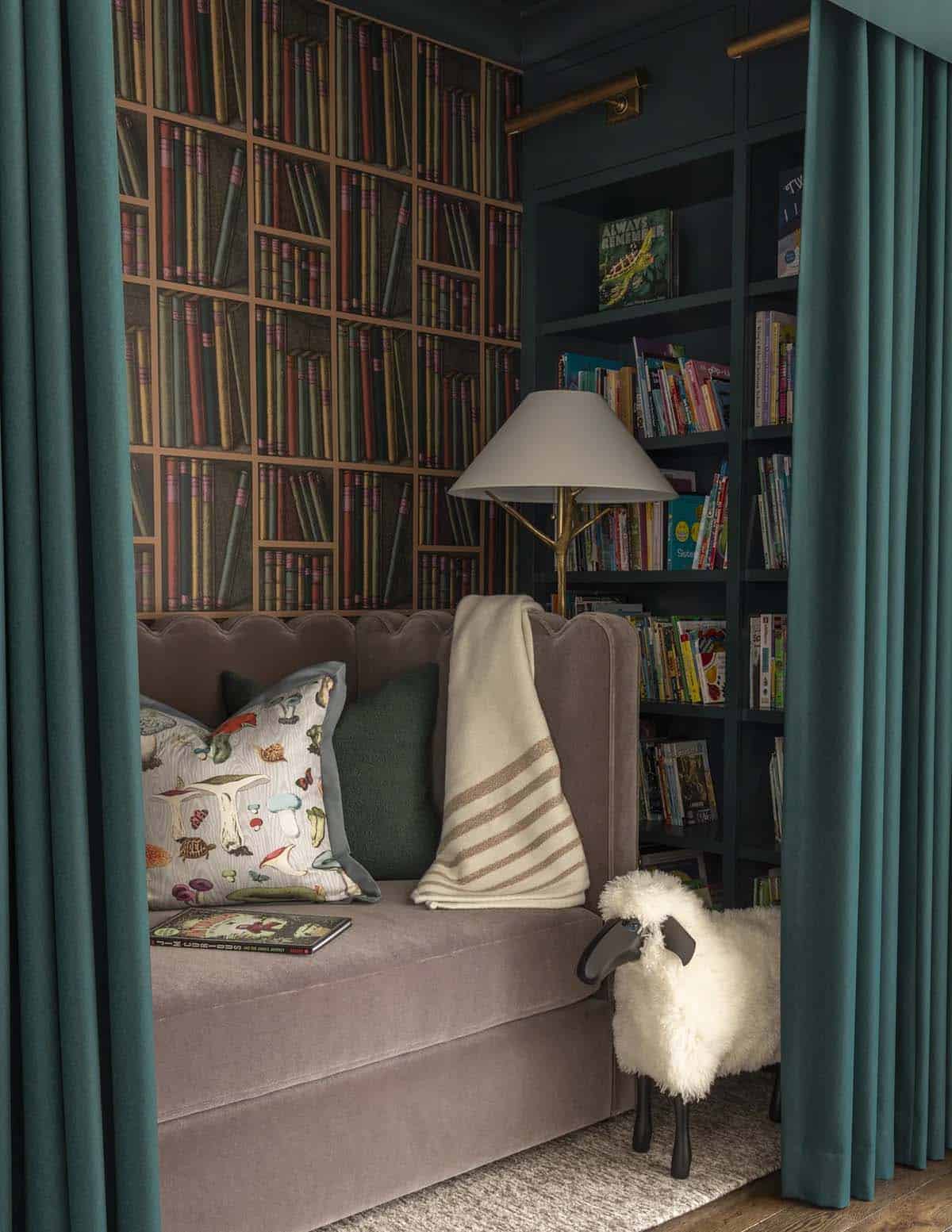 Teal curtained reading nook with bookshelf wallpaper and a sheepskin stool