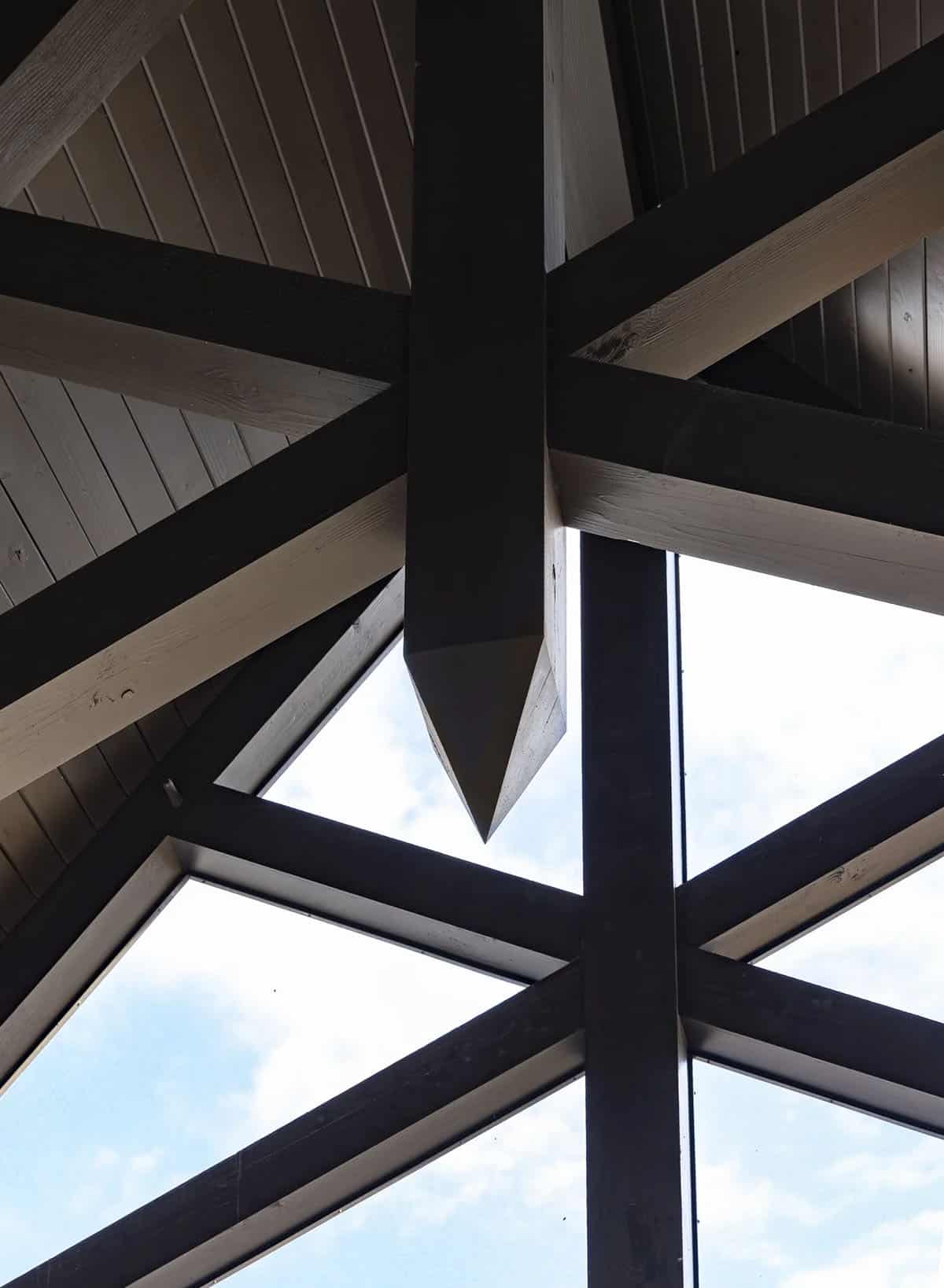 Upward view of exposed timber trusses meeting at a covered porch peak
