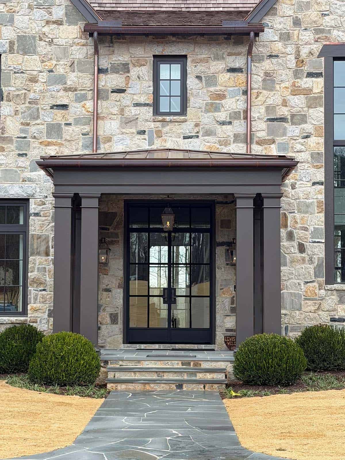 Stone entry portico with black steel double doors and copper roof