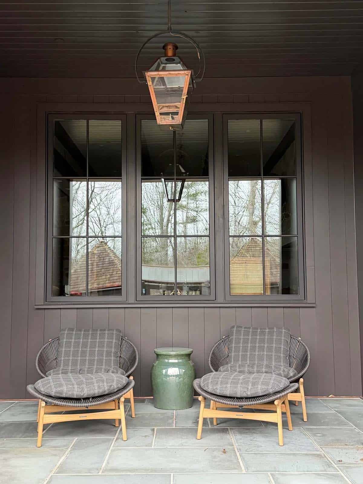 Covered porch nook with woven lounge chairs, ottomans, and a lantern light
