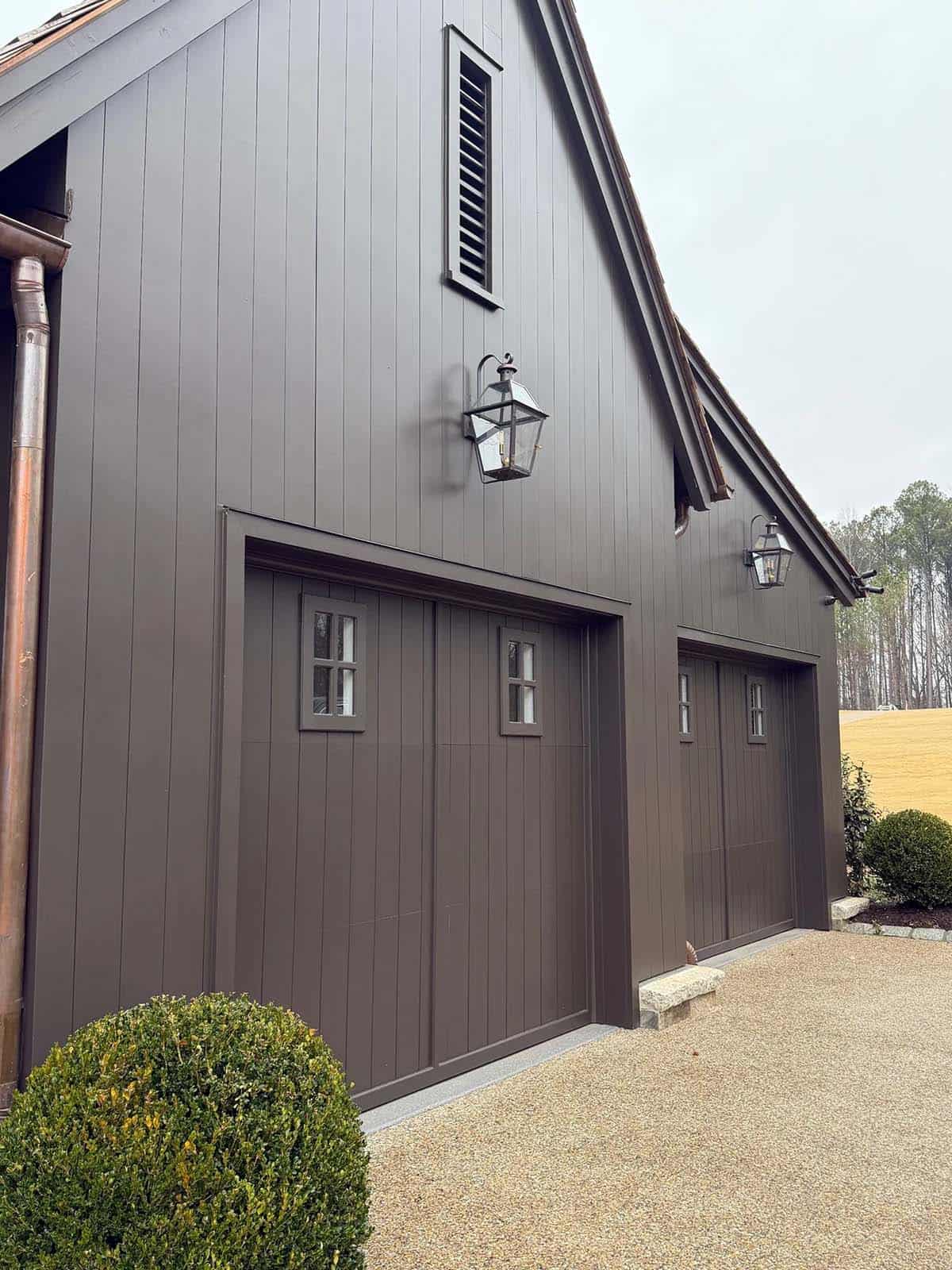 Exterior of dark board-and-batten garage with lantern sconces and copper gutters