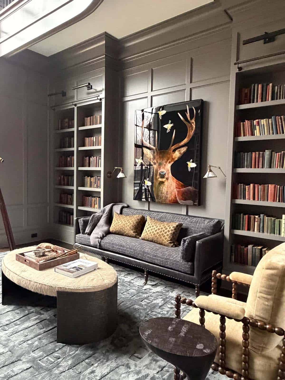 Dark library with built-in bookshelves, a nailhead sofa, and stag artwork