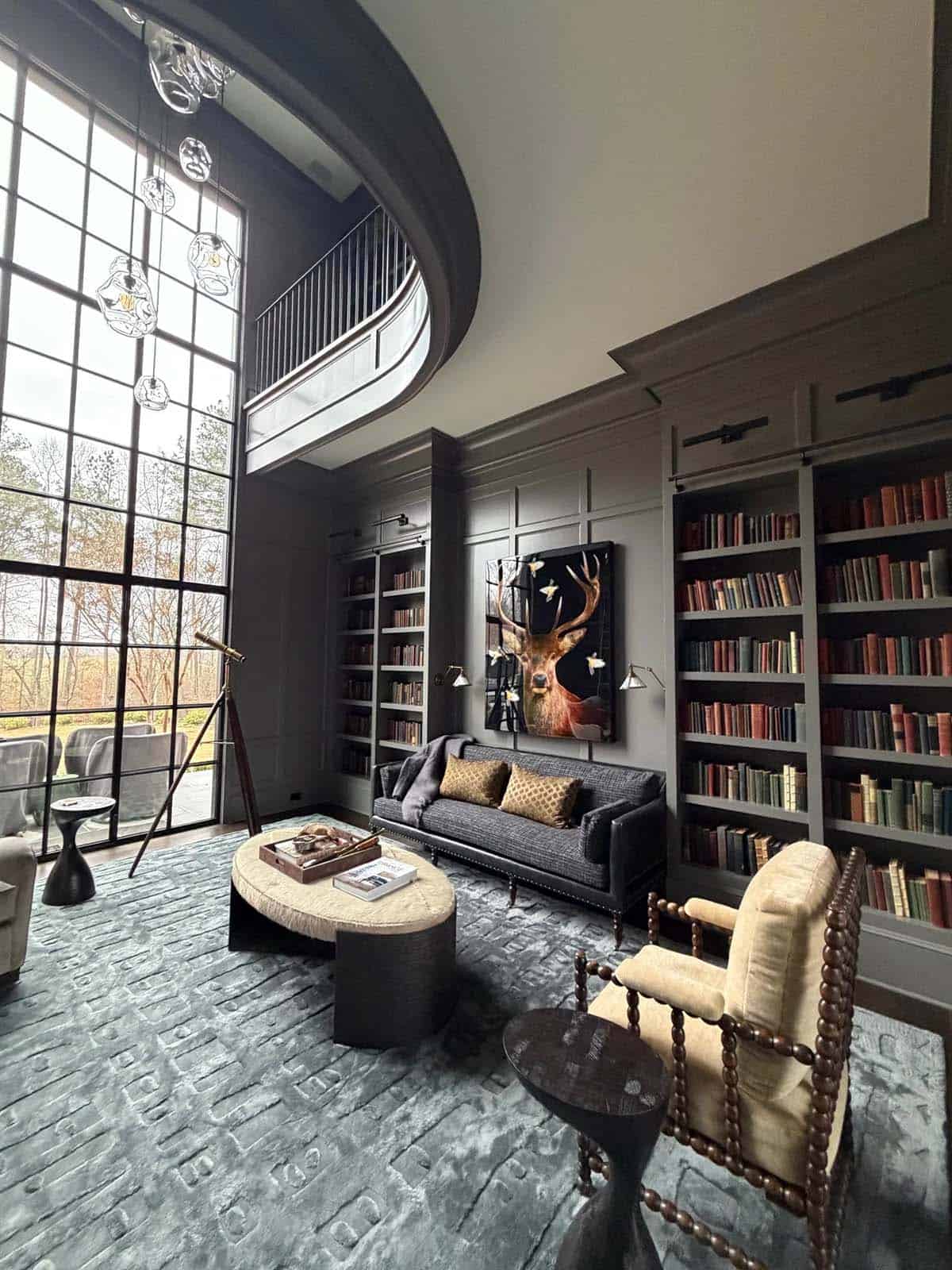 Two-story library with curved balcony railing, tall windows, and a telescope