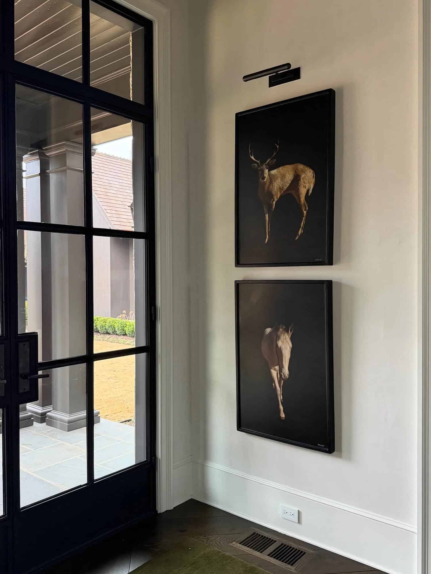 Entry hallway with framed deer and horse photography beside black steel doors