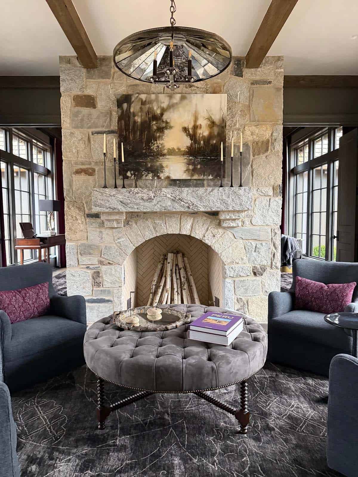 Sitting area with stone fireplace, tufted round ottoman, and mirrored chandelier