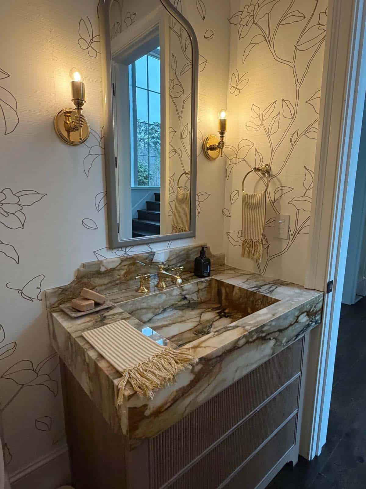 Powder room vanity with veined marble sink, brass fixtures, and floral wallpaper