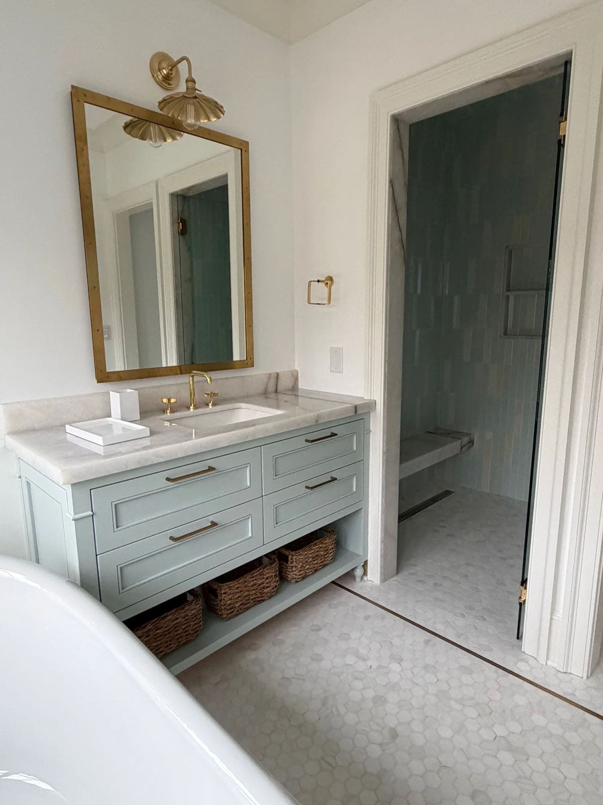 Bathroom with sage vanity, brass mirror, and view into a tiled walk-in shower