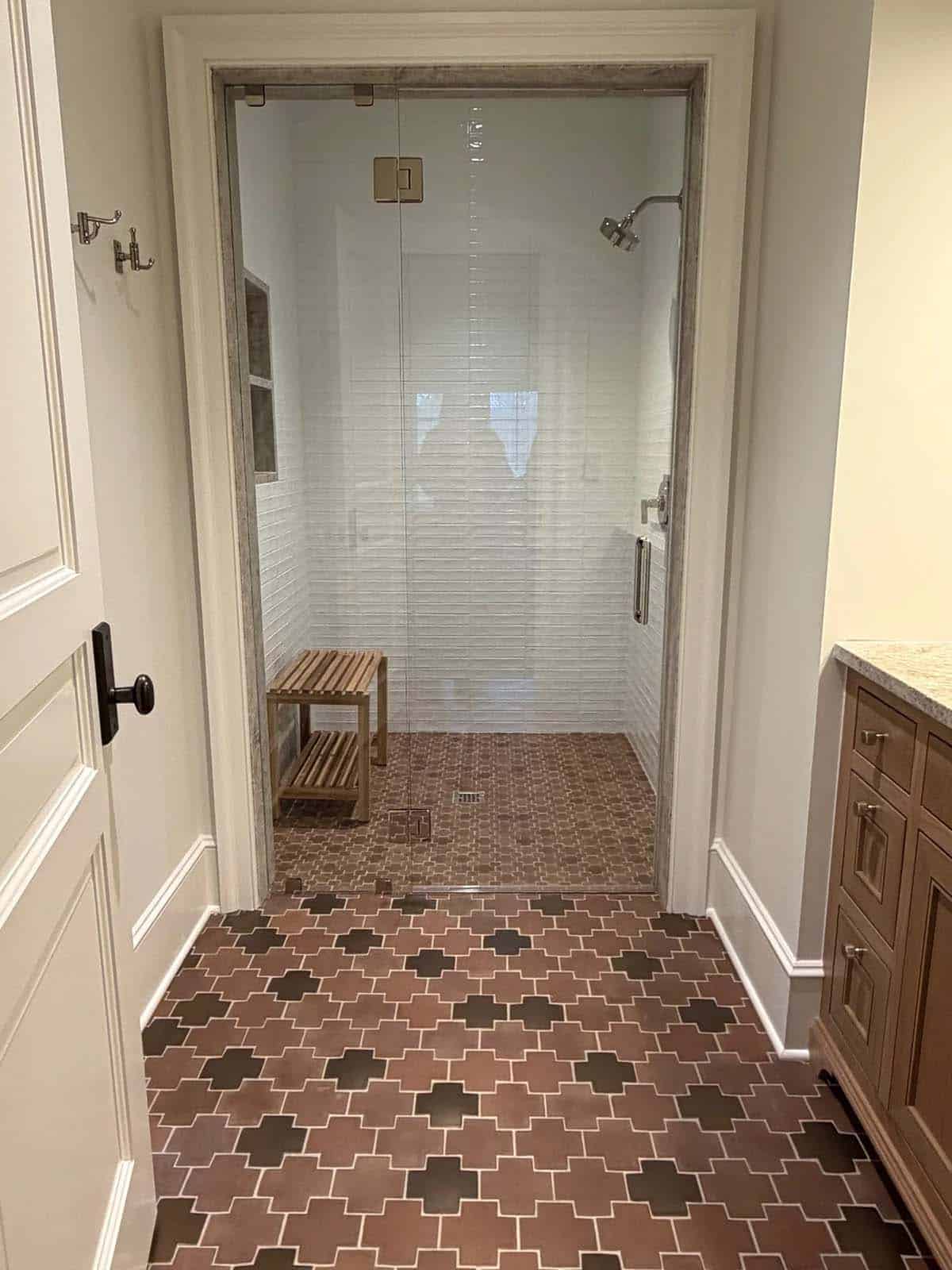 Walk-in shower with white tile, wood teak bench, and patterned floor tile