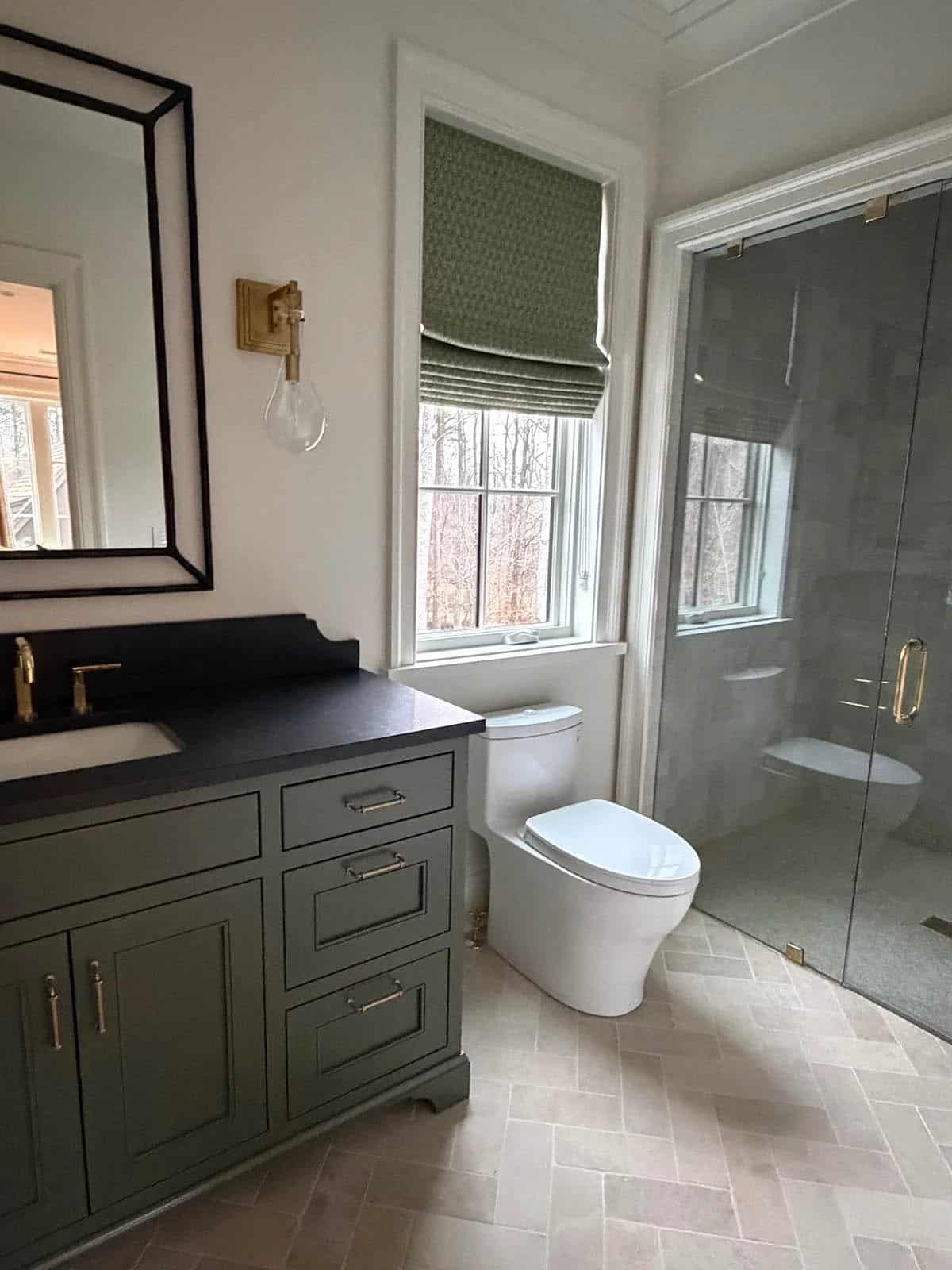 Bathroom with olive-green vanity, black countertop, and glass shower enclosure