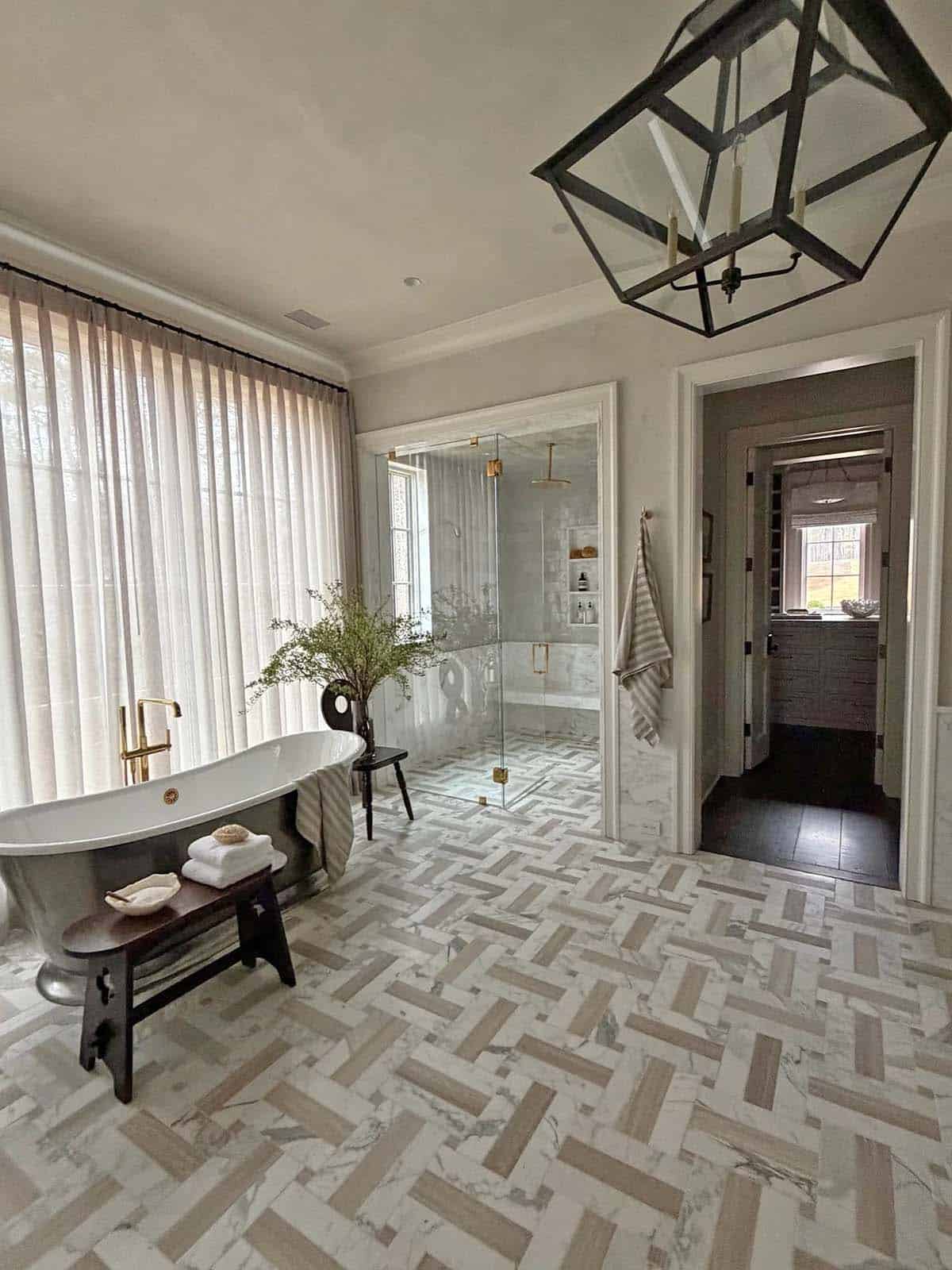 Primary bathroom with herringbone marble floor, glass shower, and lantern chandelier