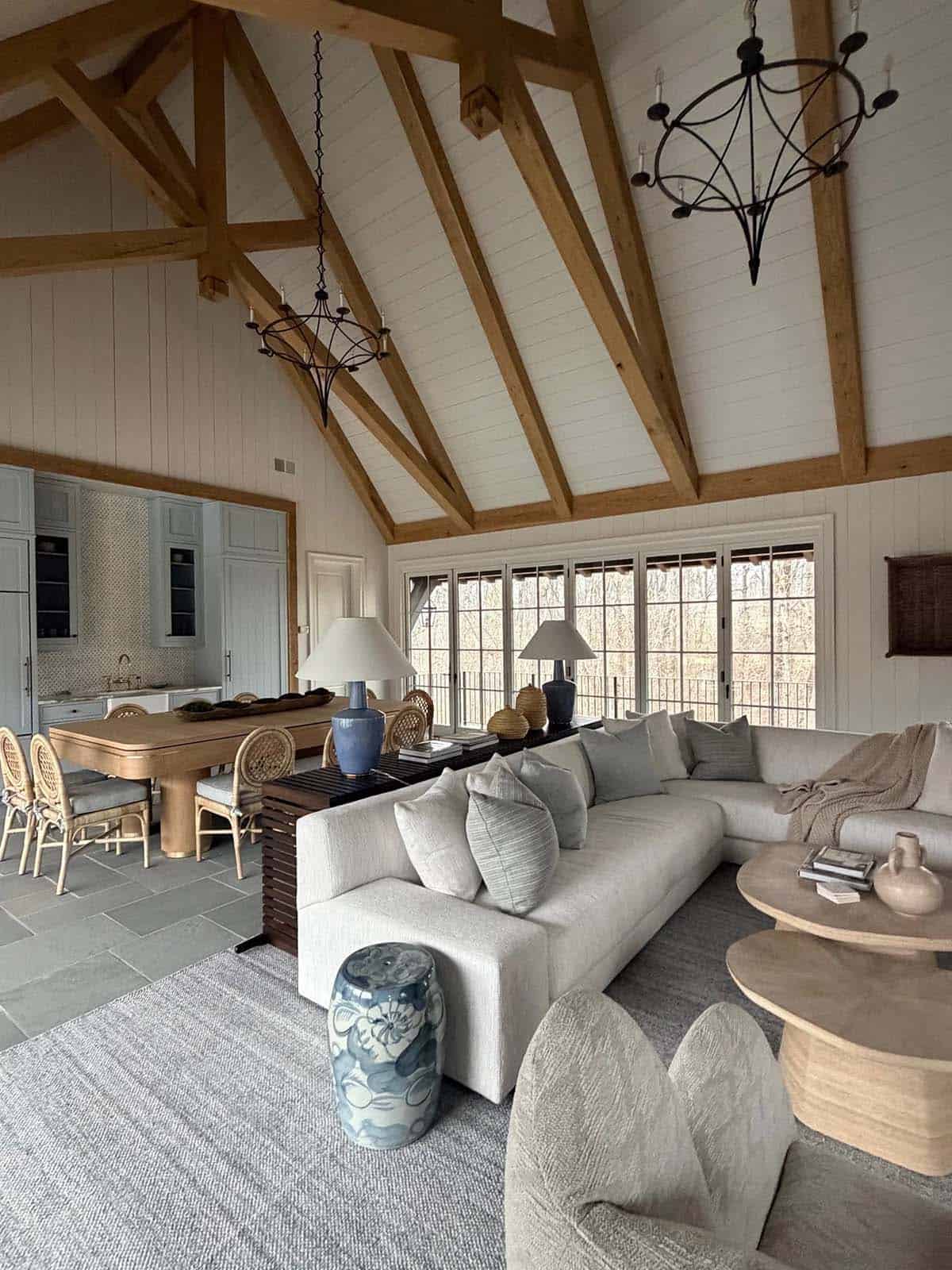 Vaulted great room with exposed timber trusses, sectional sofa, and open dining/kitchen beyond