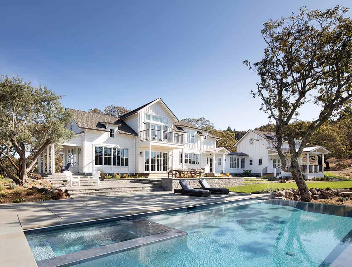Modern farmhouse exterior with white board-and-batten siding overlooking an infinity pool and stone patio