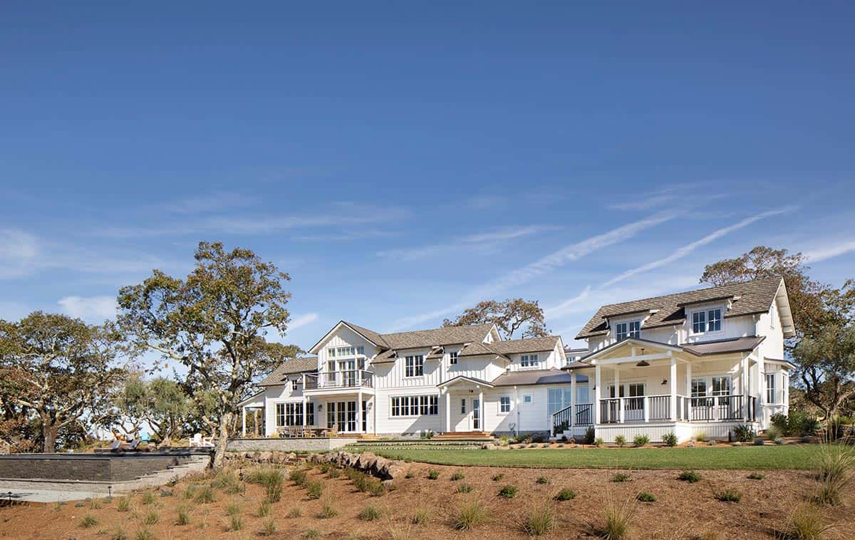 Wide exterior view of the white farmhouse compound with multiple gabled roofs and green lawn