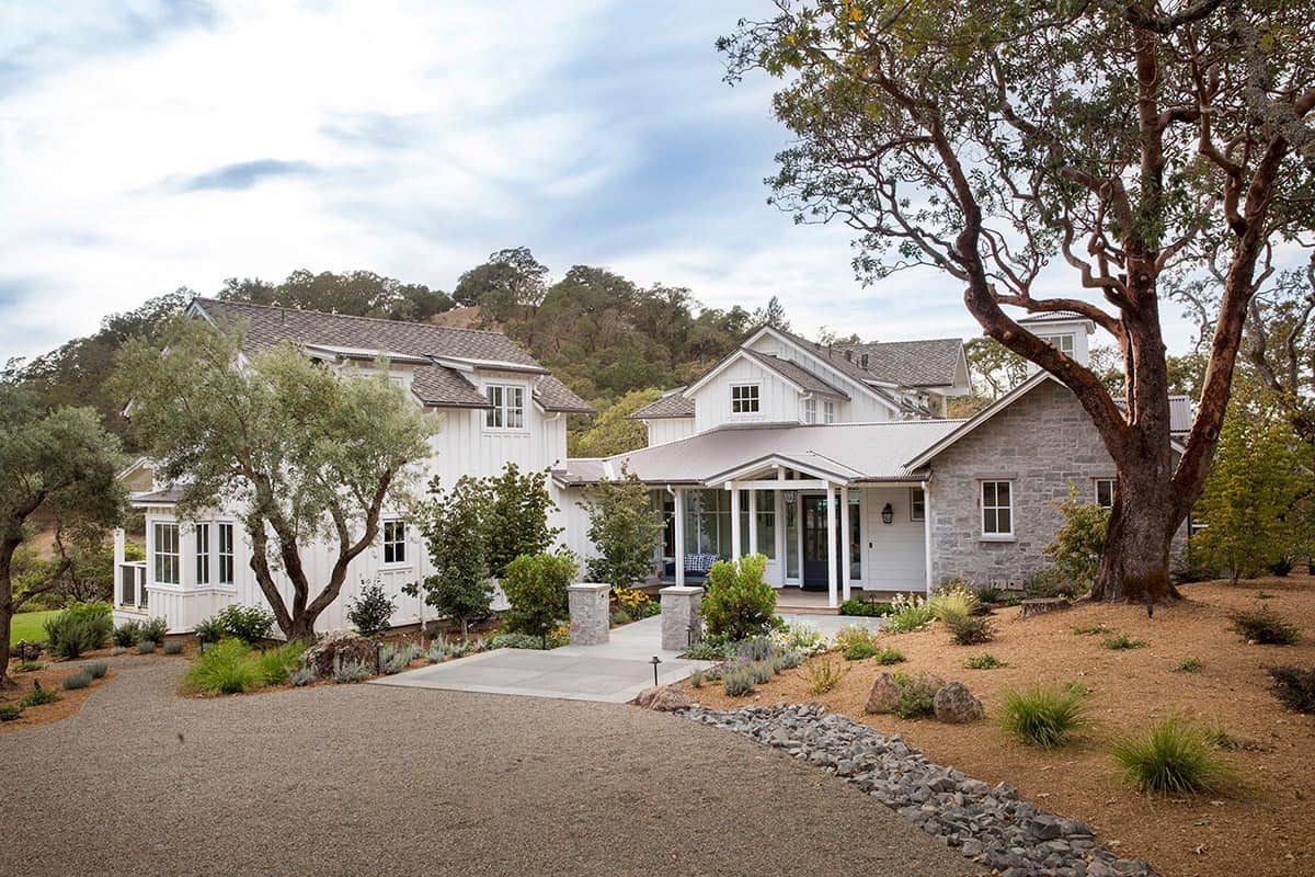 Farmhouse entrance with stone accents, gravel driveway, and covered front porch