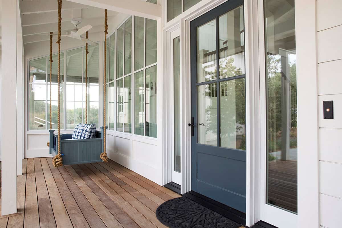 Screened porch with hanging bench swing, wood plank flooring, and blue front door
