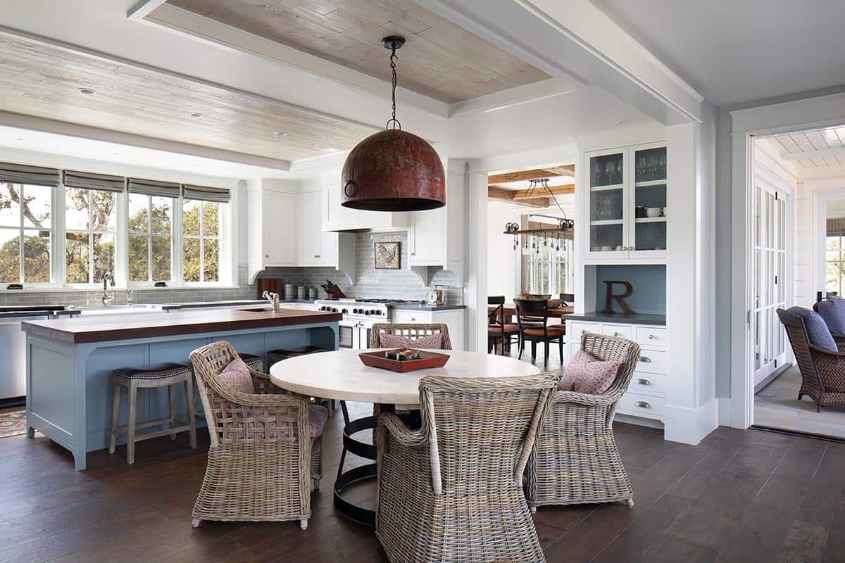 Farmhouse kitchen with blue island, round wicker dining table, and rustic red pendant light