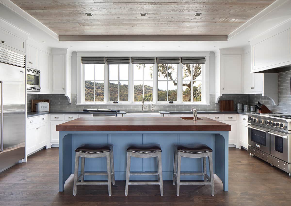 Kitchen with white cabinetry, blue island, wood ceiling, and large window over the sink